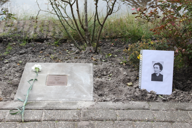 Herdenkingssteen met een witte bloem erbij en de foto van de herdachte persoon ernaast